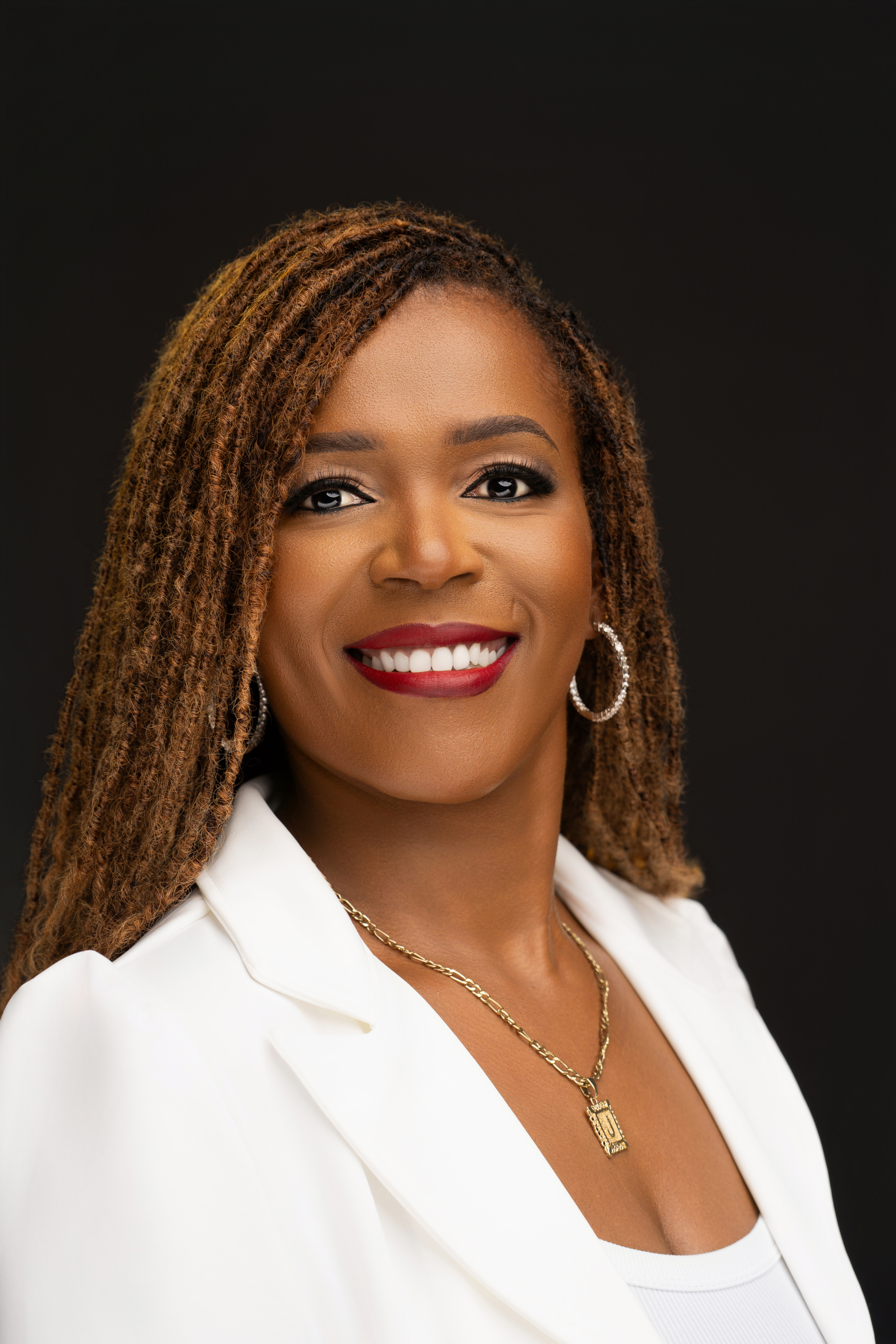 Close professional portrait of Joanne Marime in a white blazer against a black studio background