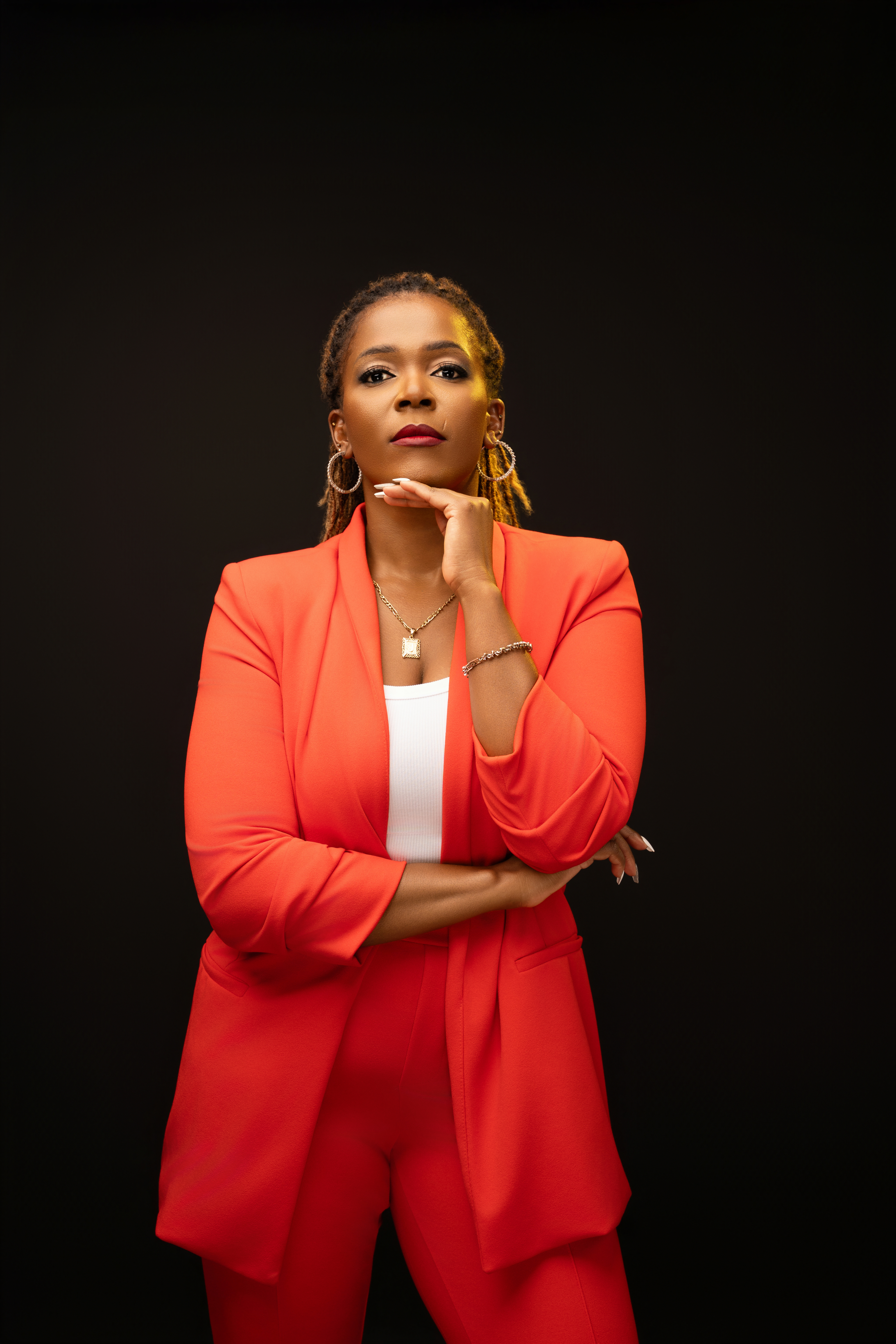 Joanne Marime posing confidently in a red-orange suit with one hand beneath her chin